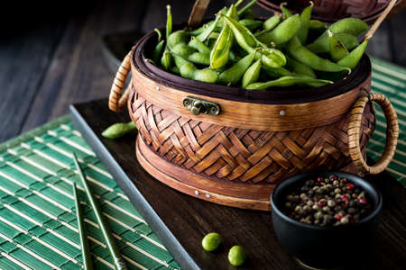 A wicker basket filled with edamame beans resting on a wooden board.の写真素材