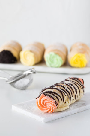 A close up of a strawberry cream cannoli topped with chocolate drizzle and other cannoli in behind.