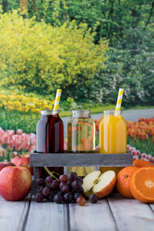 Vertical view of three bottles of fruit juice including apple, orange and grape, surrounded by fresh...