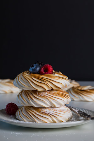 A close up of three meringues in a stack with berries on top, against a black background.の写真素材