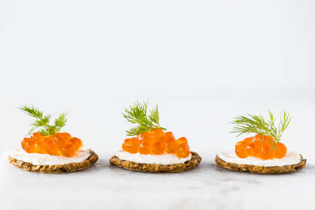 A close up view of a row of cracker and cream cheese canapes topped with red caviar and garnished with dill.の写真素材