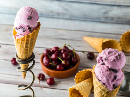 A close up view of a cherry ice cream cone in a stand with a bowl of cherries to the right.の写真素材