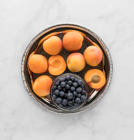 Top down view of a metal tray of apricots and a small bowl of blueberries. A complimentary colour concept. の写真素材