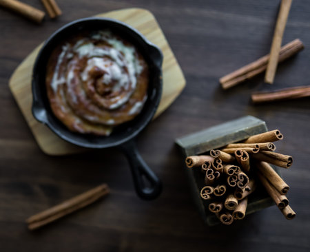 A top down view of a cinnamon bun in soft focus with selective focus on a box of cinnamon sticks.