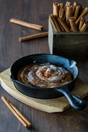A close up view of a cinnamon bun baked in a cast iron frying pan cooling on a wooden trivet.の写真素材