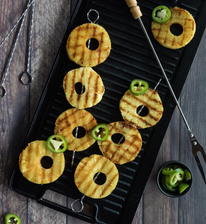 A top down view of grilled pineapple skewers with jalapenos on a grill pan against a dark background.の写真素材