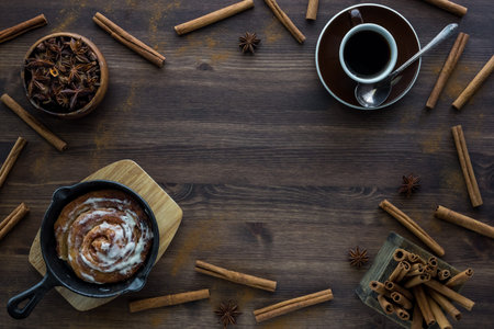A top down view of a border of cinnamon sticks, coffee and a cinnamon bun. Coffee break concept.