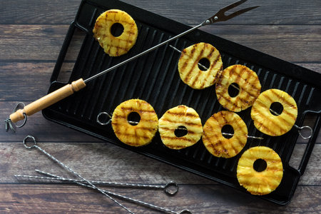 A top down view of grilled pineapple rings on metal skewers on a grill pan.の写真素材