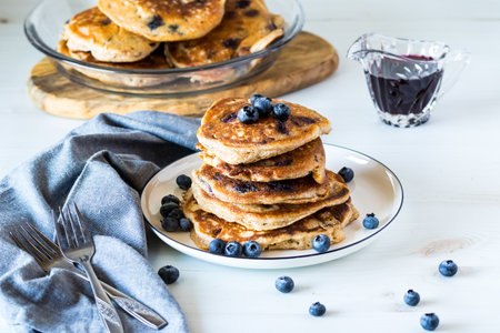 Blueberry pancakes stacked on a plate with blueberry syrup, ready for eating.