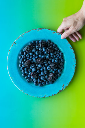 hand holding a bright blue plate of blueberries and blackberries against a vibrant background.