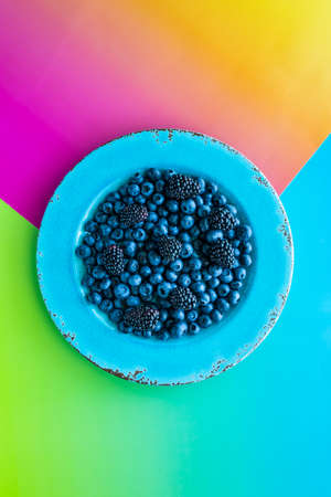 Blueberries and blackberries on a bright blue plate against a vibrantly colourful background.の写真素材