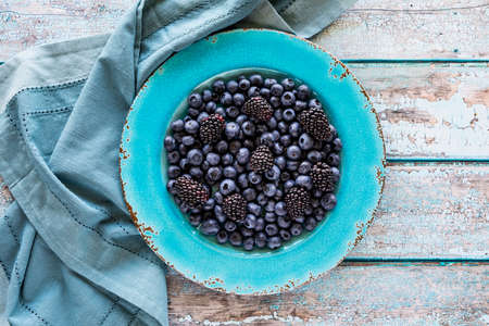 Blueberries and blackberries on a vibrant blue plate against a wooden background.の写真素材