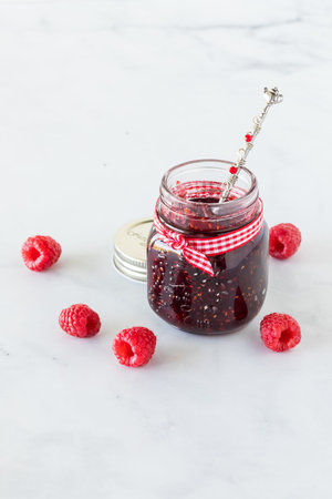 Small jar of raspberry jam surrounded by fresh raspberries.
