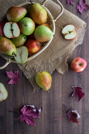 Top down view of a basket filled with apples and pears surrounded by dried leaves. Autumn concept.