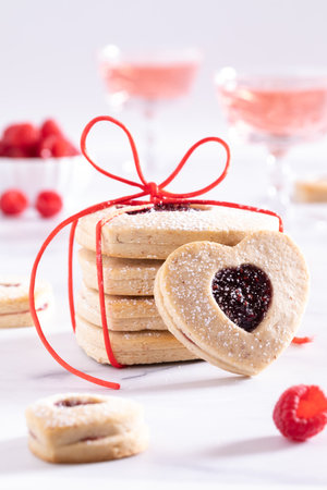 A stack of heart shaped Linzer cookies with one in front and sparkling juice in behind against a bright background.の写真素材