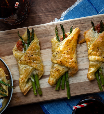 Close up of asparagus and prosciutto pastry bundles fresh out of the oven with two glasses of soda.の写真素材