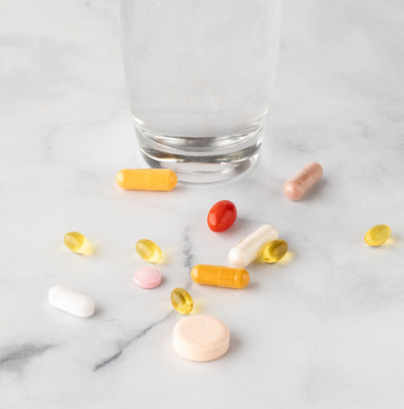 Vitamins and supplements scattered on a table with a glass of water in behind.の写真素材