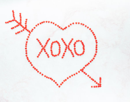 Top down view of red cinnamon hearts in the shape of a heart with XOXO, the symbol for hugs and kisses in the middle.の写真素材