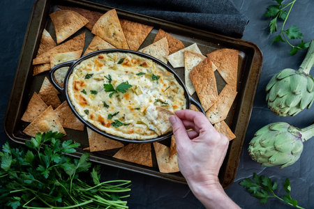 Top down view of a hand dipping a pita triangle into a warm artichoke dip.の写真素材