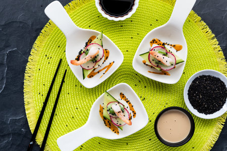 Top down view of deconstructed sushi with black sesame seeds and dipping sauces on a bright green...