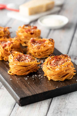 Spaghetti nest appetizers on a wooden board sprinkled with parmesan cheese.の写真素材