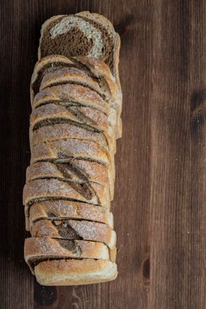 Top down view of a loaf of marble rye bread cut into slices on a wooden table.