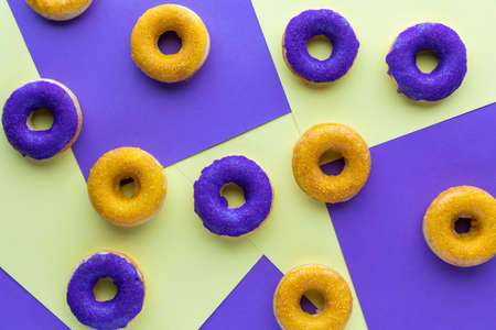 Top down view of an assortment of purple and yellow donuts on purple and yellow paper sections.の写真素材