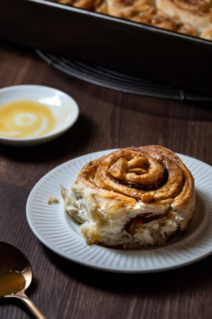 Close up of a homemade cinnamon bun topped with caramel sauce on a plate on a dark wooden table.の写真素材