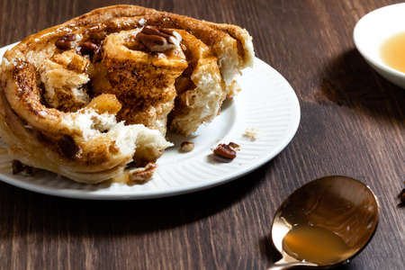 Close up of a homemade cinnamon bun topped with caramel sauce and crushed pecans, broken open to show the inner spiralの写真素材