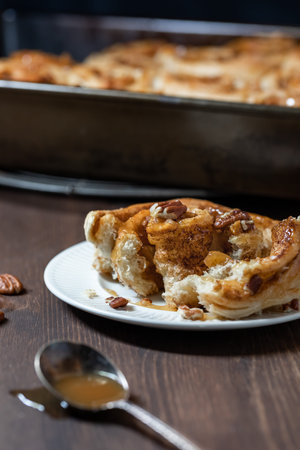 Close up of a cinnamon bun torn open and topped with caramel sauce and pecan nuts.の写真素材