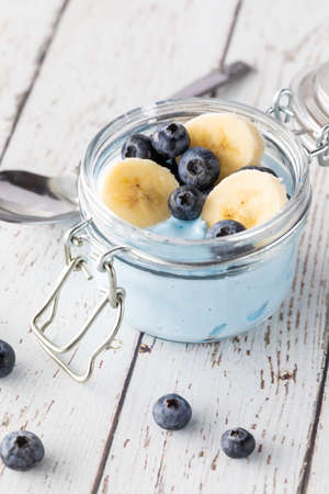 Close up view of a blue spirulina yogurt jar topped with fresh blueberries and banana slices.の写真素材