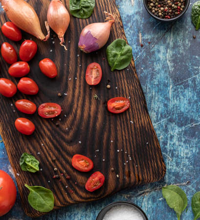 Top down view of a wooden cutting board with sliced cherry tomatoes and shallots.の写真素材