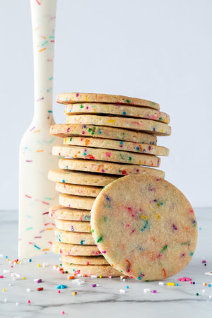 A stack of sprinkle sugar cookies with a sprinkle designed rubber spatula standing beside and sprinkles scattered.の写真素材