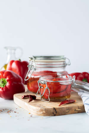Close up of jars of roasted red peppers on a wooden cutting board against a light background.の写真素材