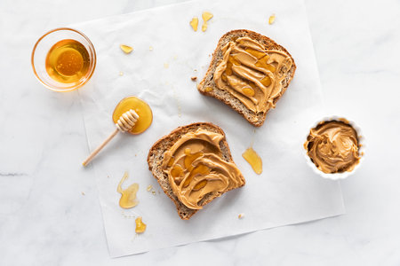 Two pieces of toast with peanut butter and honey spread on top and a mess of honey all around.の写真素材