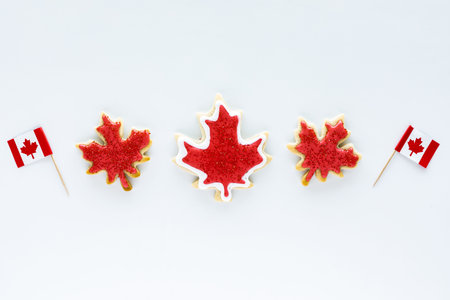 A row of Canada flag sugar cookies with two mini Canada flag picks isolated against a white...