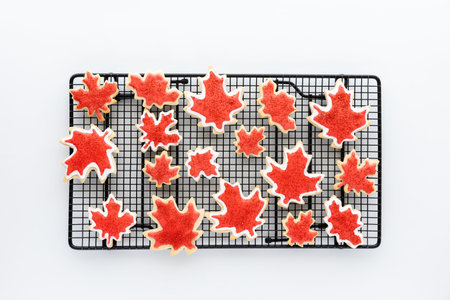 A cookie sheet topped with many different shapes and sizes of Canada flag sugar cookies against a...