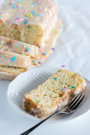 A serving of confetti loaf cake with the sliced loaf on parchment paper in behind.