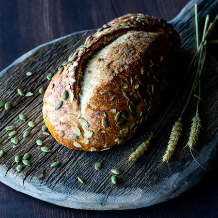 Close up view of a loaf of pumpkin seed bread on a rustic wooden board against a dark background.の写真素材