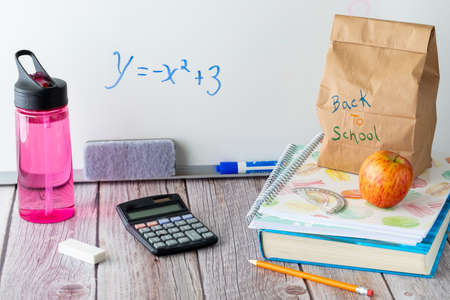 Straight on view of a table top scene of school supplies including lunch and water bottle, against a white board. Back to school concept.の写真素材