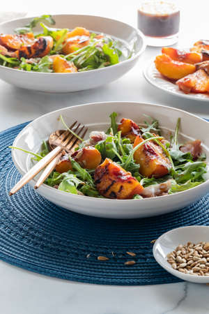 Close up of a grilled peach and arugula salad garnished with sunflower seeds, lit from the back.の写真素材
