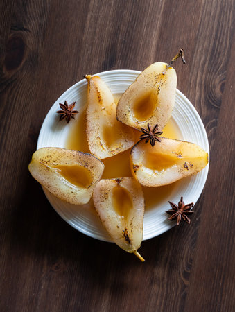 Top down view of a poached and torched pears with star anise on a dark wooden table.