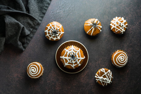 Top down view of various cupcakes decorated for Halloween, scattered about against a dark background.の写真素材