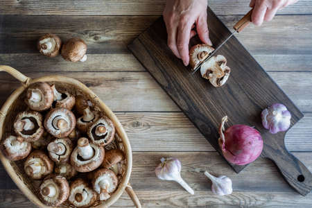 Hands cutting mushrooms on a wooden cutting board.の写真素材