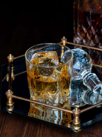 A glass of whiskey on a glass tray, against a black background.の写真素材