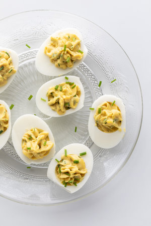 Top down view of a decorative glass plate of creamy deviled eggs, ready for eating.