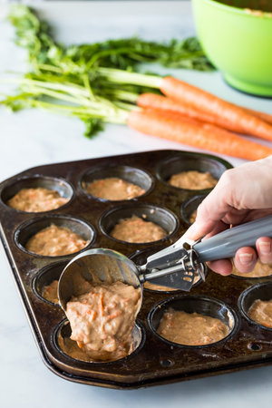 Carrot cake muffin batter being scooped into a muffin tin for baking.の写真素材