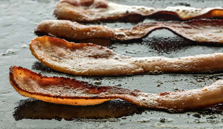 Crispy strips of bacon frying on a cast iron griddle pan.の写真素材