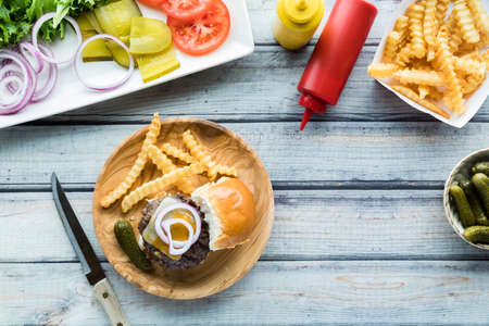 A cheeseburger slider on a wooden plate served with french fries.の写真素材