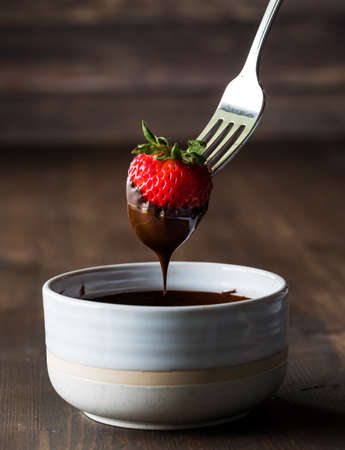 Close up of a strawberry dipped in melted chocolate, against a dark background.の写真素材